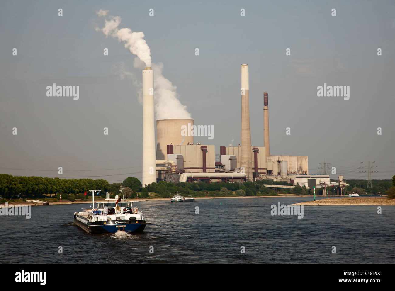 Lastkähne schlängeln sich unten der Fluss Rhein, Deutschland, indem man ein Kernkraftwerk. Stockfoto