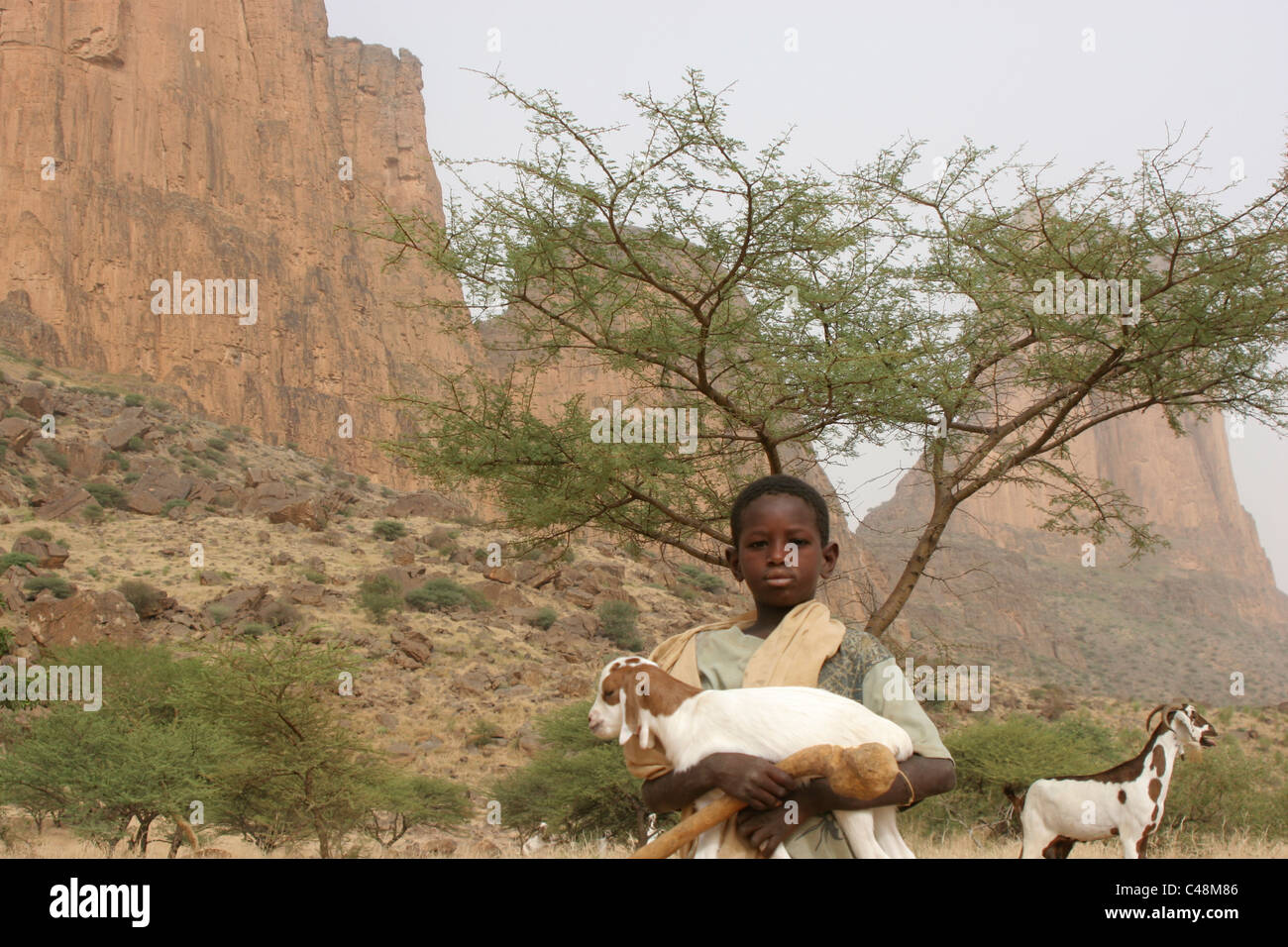 Ein Hirtenjunge afrikanischen Fulbe hält ein Zicklein mit der Hand von Fatima in den Hintergrund, Hambori, Mali, Westafrika Stockfoto