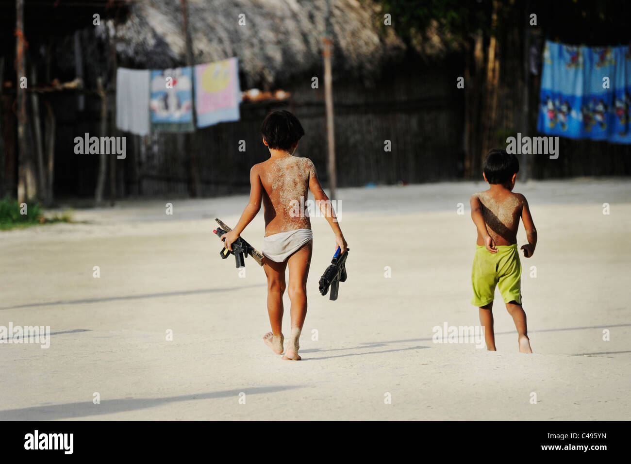 Kuna-Kinder Fuß über den Hauptplatz in Nalunega mit Spielzeugpistolen, San Blas Inseln, Panama Stockfoto