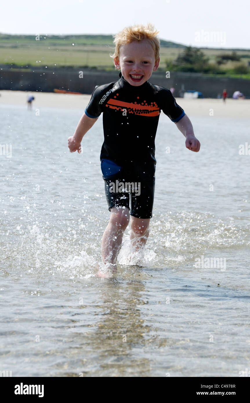 Ein kleiner Junge läuft durch das Meer, lächelnd und Spritzwasser. Stockfoto