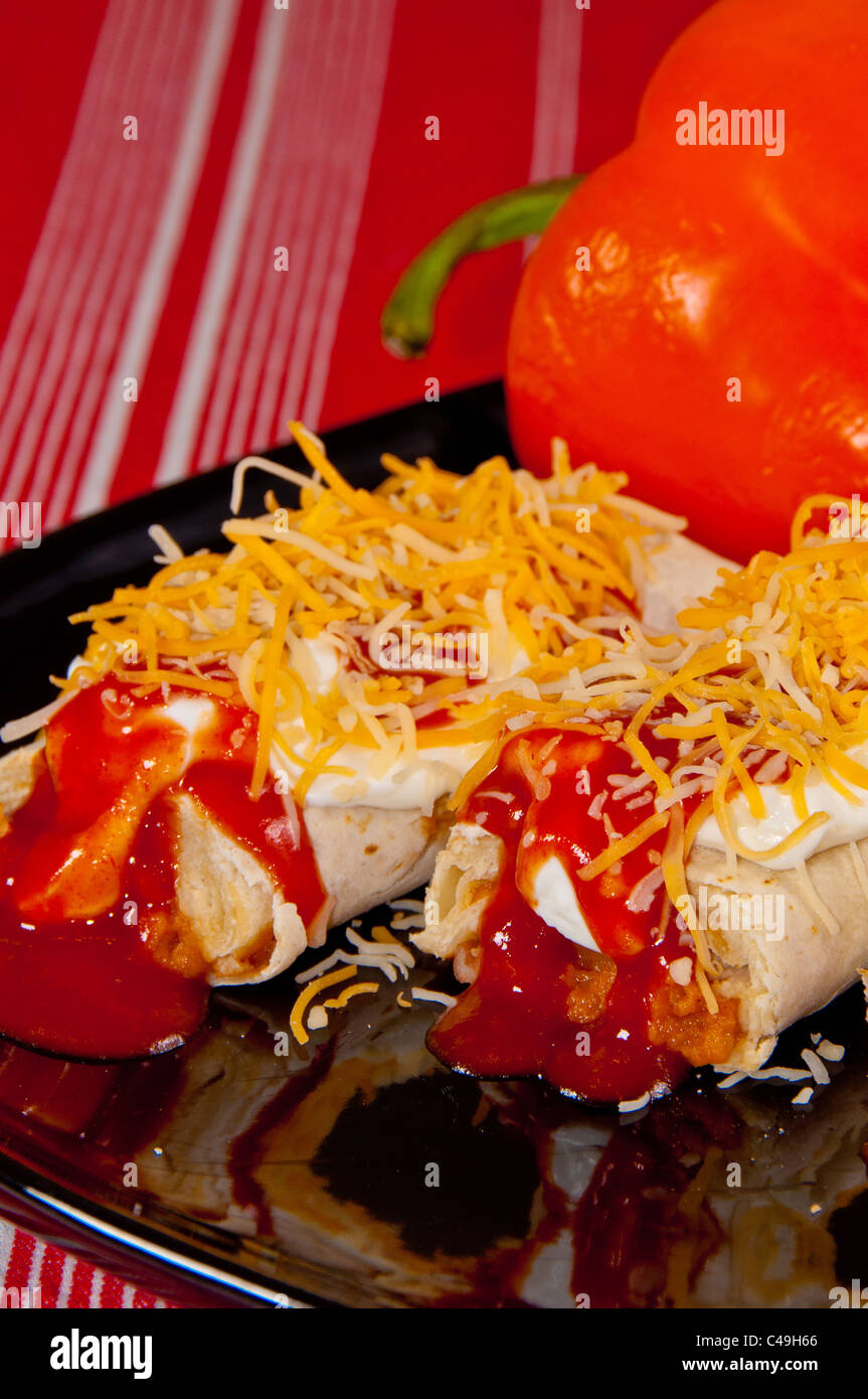 Zwei Burritos mit Sauerrahm, Enchiladasoße und geschreddert Käse auf einem schwarzen Schild auf einem roten Tuch bedeckt. Stockfoto