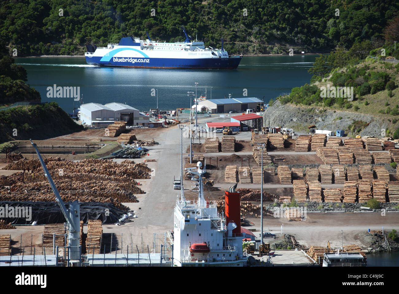 Holz aufgestapelt am Kai im Hafen Marlborough, in der Nähe von Picton, Neuseeland mit einer Bluebridge Fähre ankommen im Hintergrund. Stockfoto
