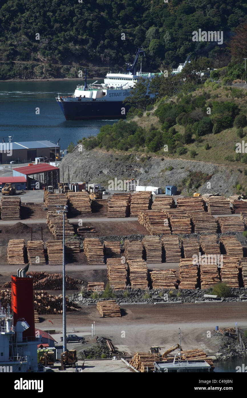 Holz gestapelt am Kai im Hafen Marlborough, in der Nähe von Picton, Neuseeland mit einer Bluebridge Fähre ankommen im Hintergrund Stockfoto