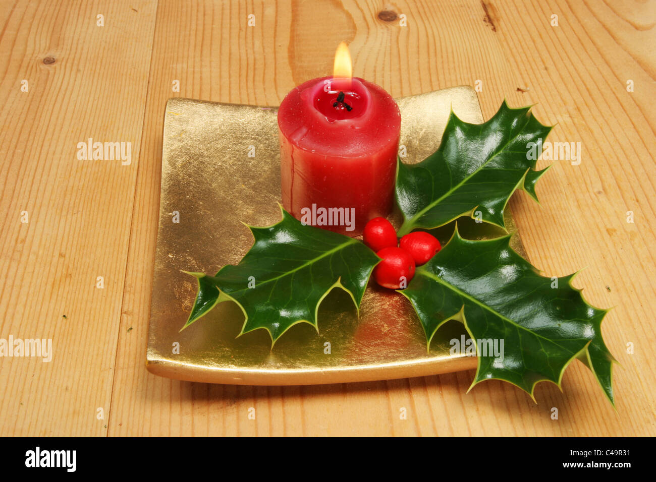 Brennende rote Kerze und Stechpalme mit Beeren Stockfoto