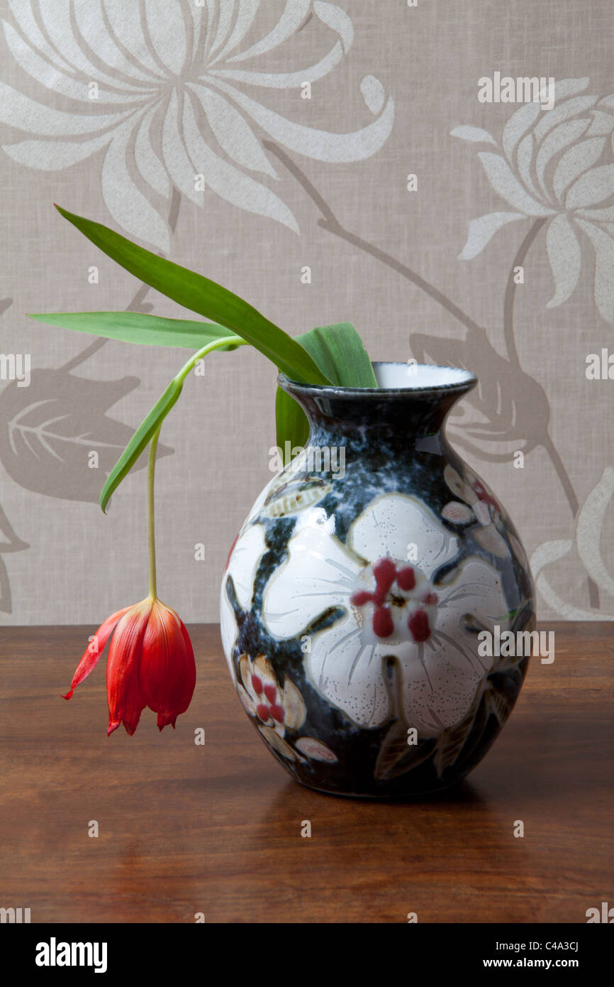 Hängende rote Tulpe in verzierte Vase auf Tischplatte. Stockfoto