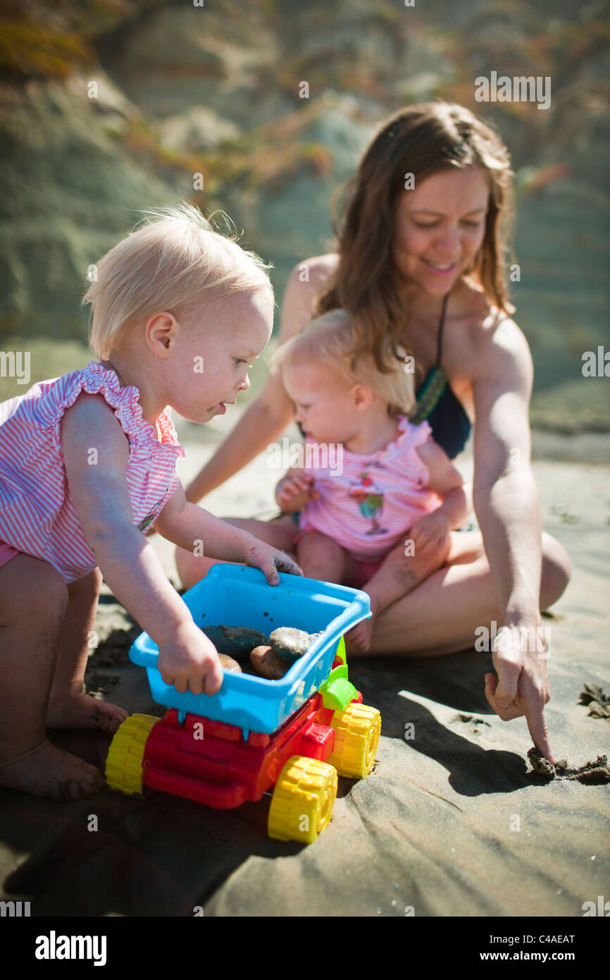 Mutter spielt mit einjähriger eineiigen Zwilling Girls am Strand Stockfoto