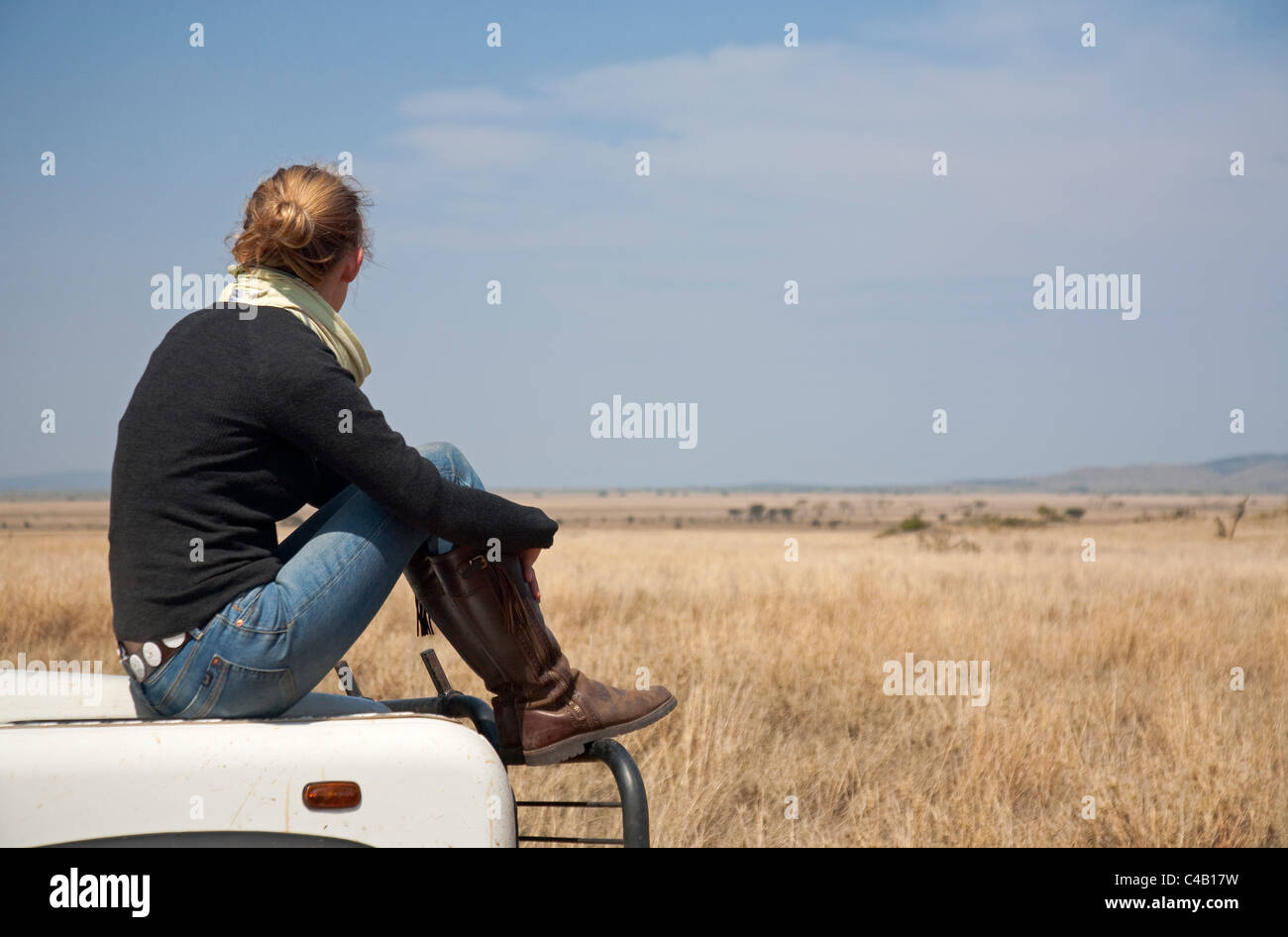 Tansania, Serengeti. Eine Frau blickt auf die Serengeti Plains von der Motorhaube von ihrem Land Rover. MR. Stockfoto