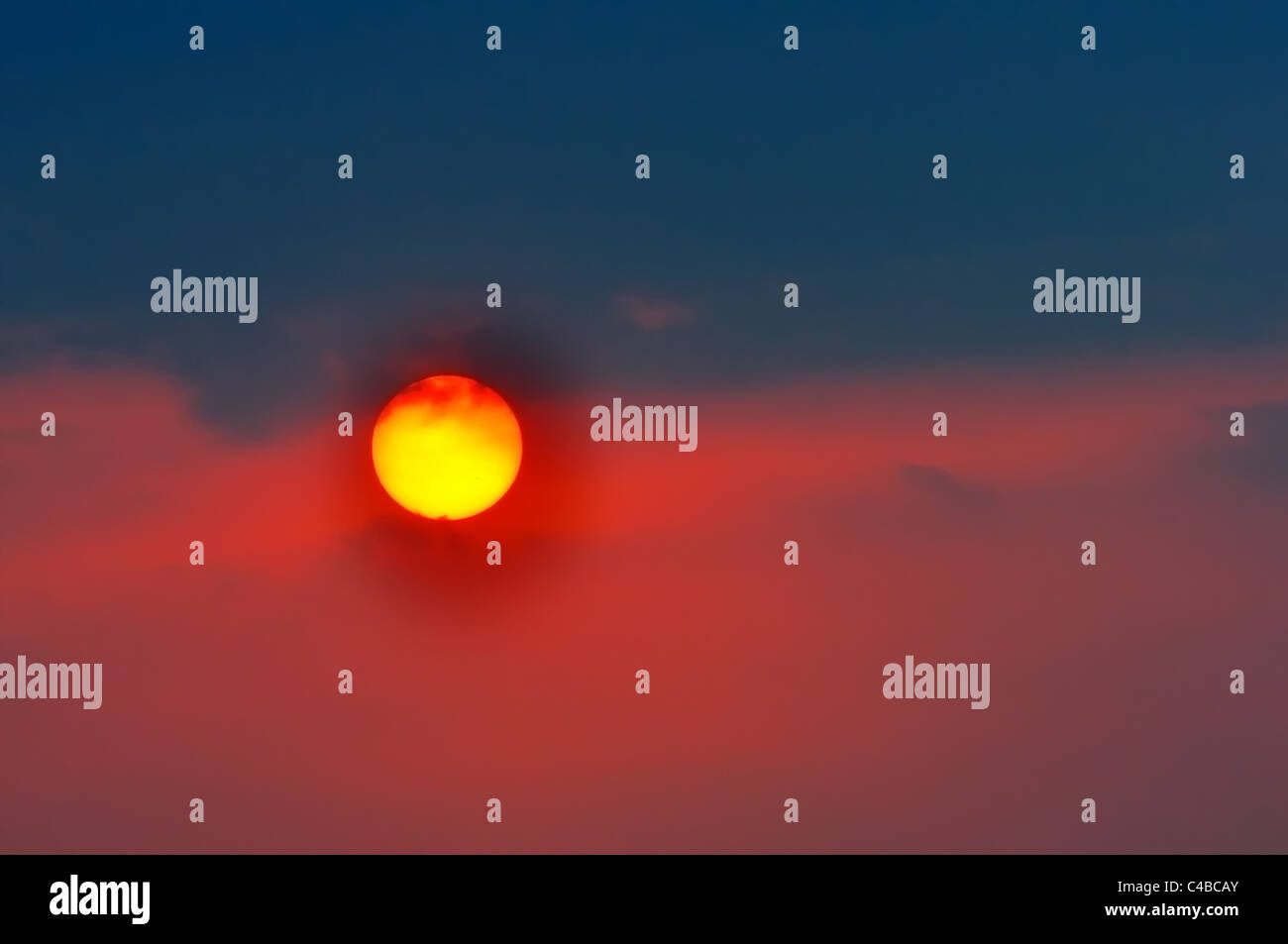 Die untergehende Sonne mit Wolken rot und bläulich schwarz gefärbt Stockfoto