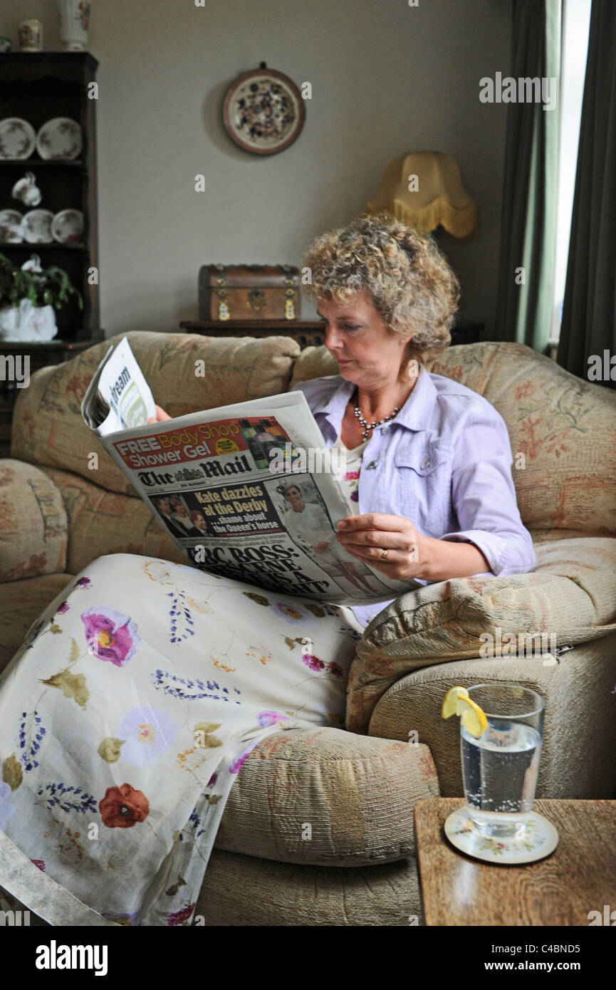 Frau mittleren Alters Lesen der Post am Sonntag British National Zeitung zu Hause UK nach Modell gestellt Stockfoto