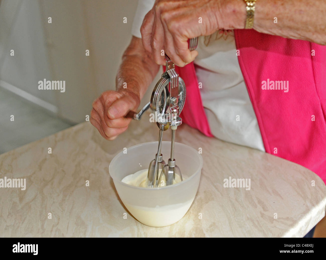 Frau mit einer alten altmodischen Hand Schneebesen in einer Schüssel Sahne in Küche UK Stockfoto