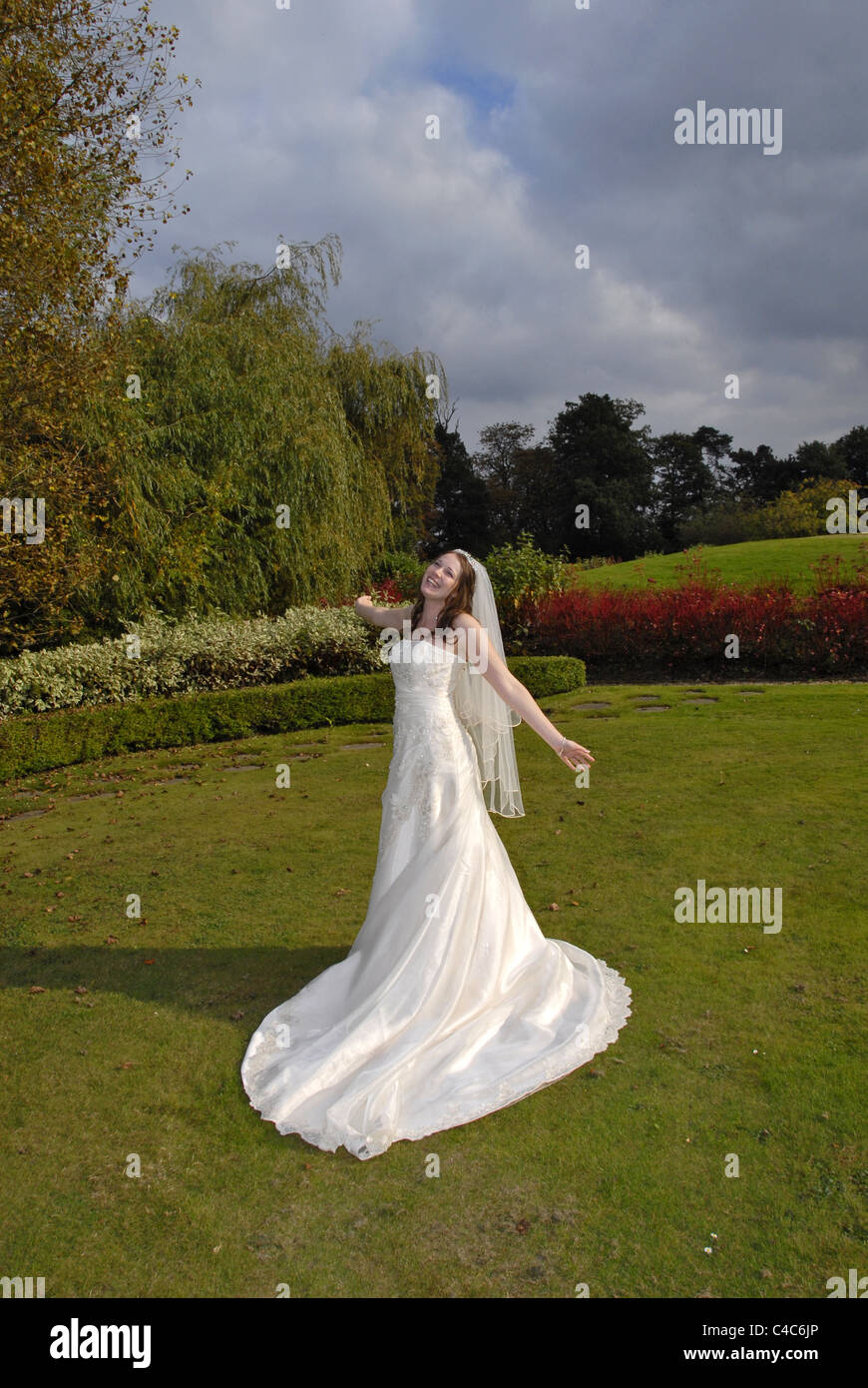Portraitbild einer schönen Braut in ihrem Hochzeitskleid und Schleier hindurch drehte und in farbenfrohen Gärten frei fühlen Stockfoto