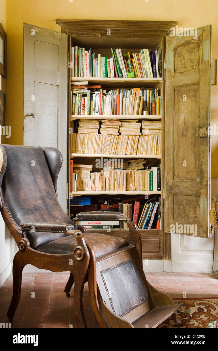 Antiken hölzernen Ohrensessel Sessel mit Lederbezug und Fußstütze in Zimmer mit rustikalen Französisch offene Holzschrank mit Büchern Stockfoto