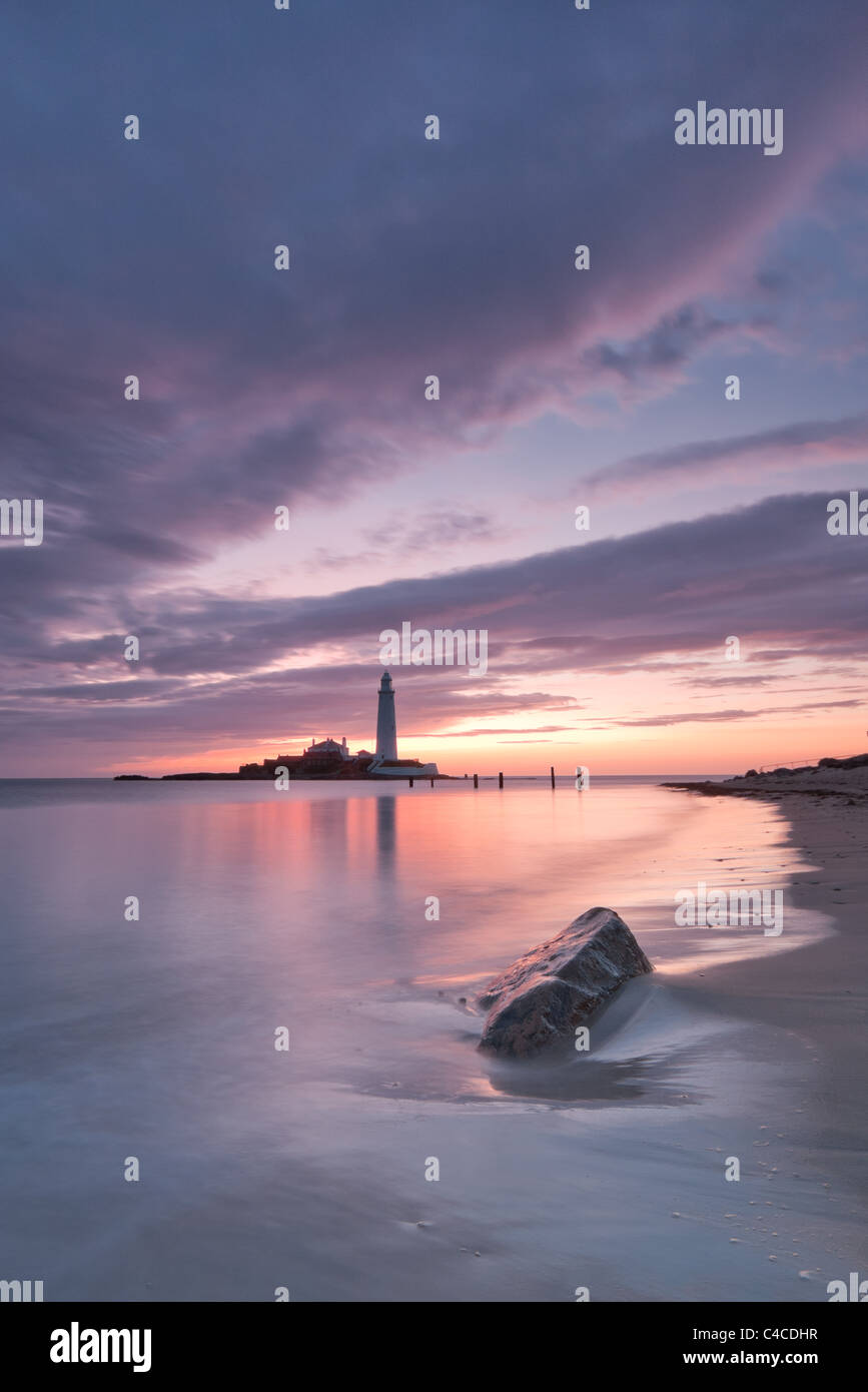 Golden Dawn Licht reflektiert auf ruhiger See führt zu einem Leuchtturm am Horizont mit Rock Detail im Vordergrund Stockfoto