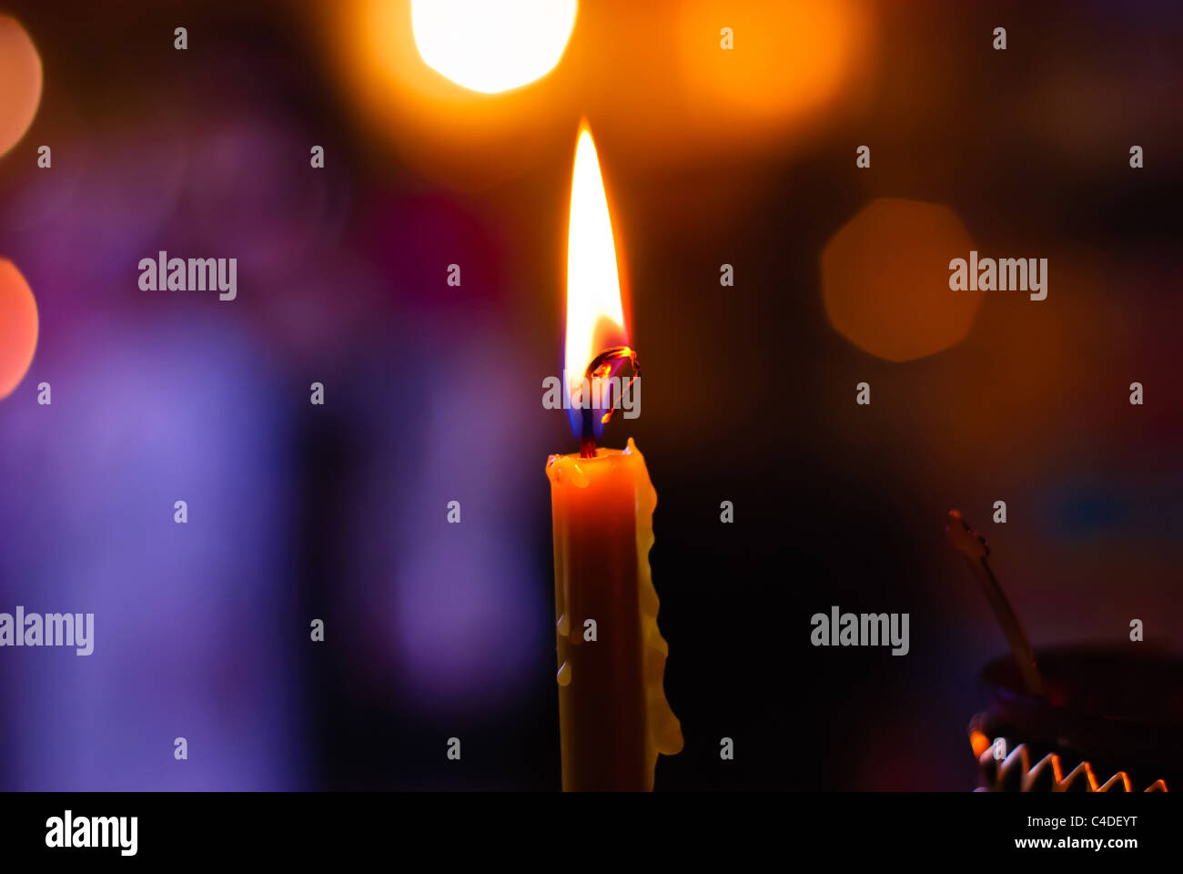 Brennende Kerze auf einem unscharfen farbigen Hintergrund Stockfoto