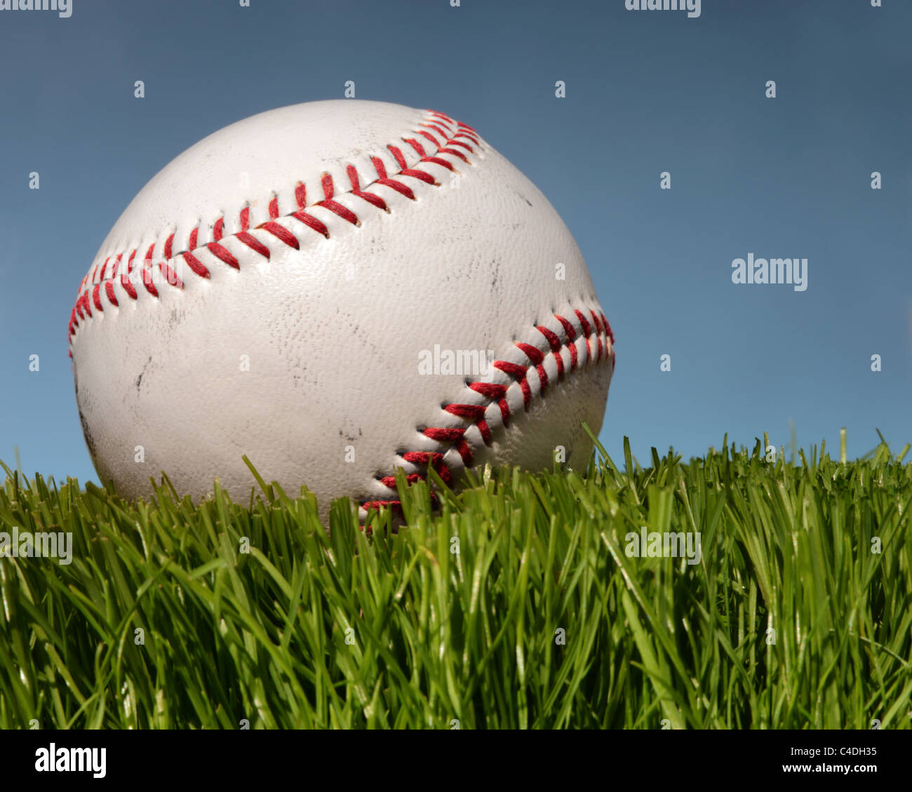Baseball auf dem grünen Rasen mit blauen Himmel dahinter. Stockfoto