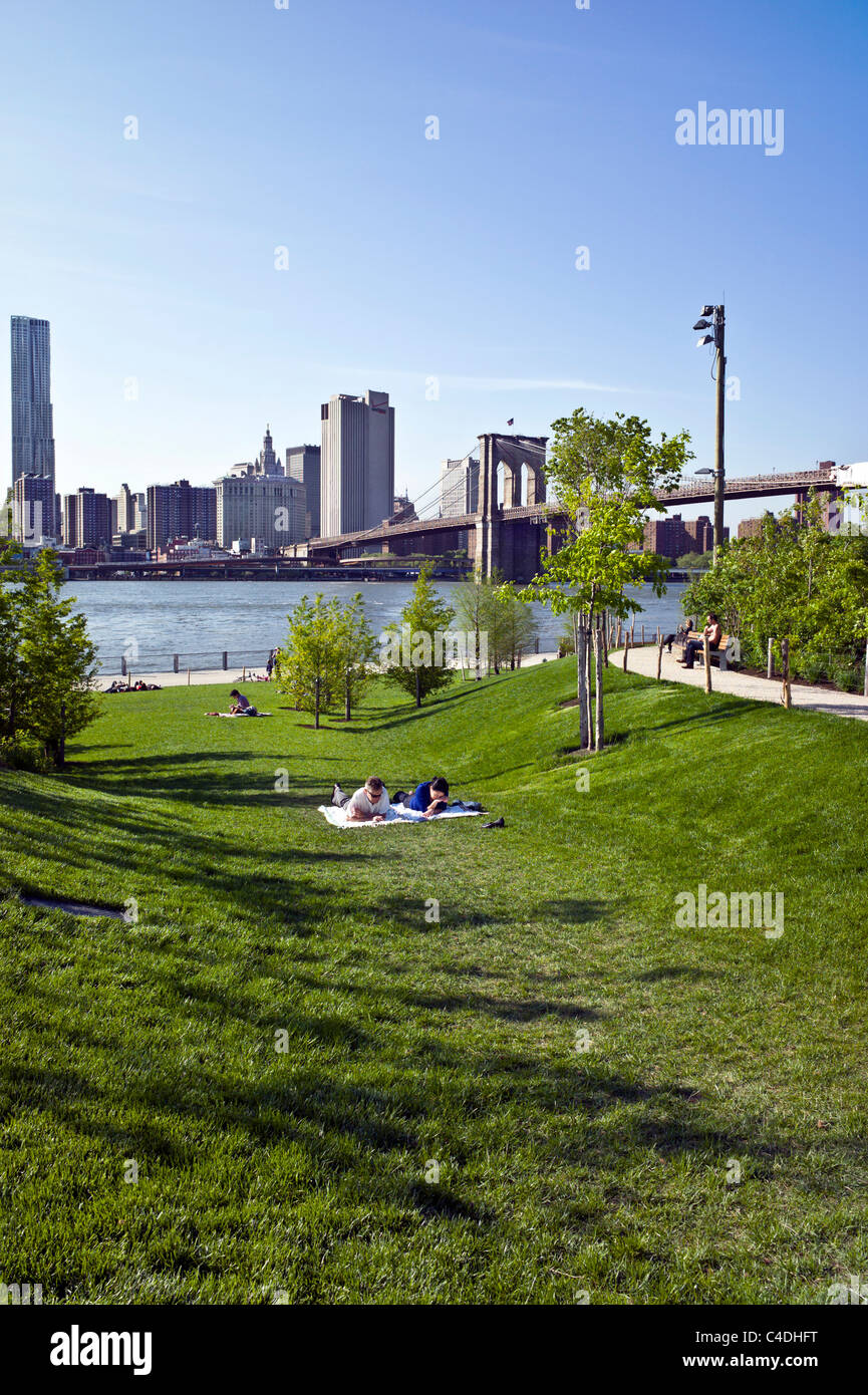 Menschen entspannen Sie auf abfallende Rasenfläche im Brooklyn Bridge Park mit Blick auf Esplanade East River & Lower Manhattan skyline Stockfoto