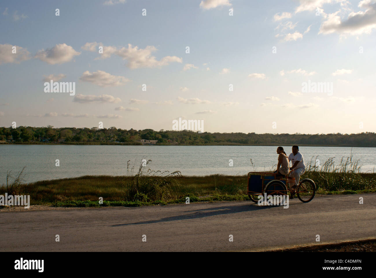 Paar auf einem Dreirad mit Lake Coba oder Laguna Cobá im Hintergrund, Coba, Quintana Roo, Mexiko Stockfoto