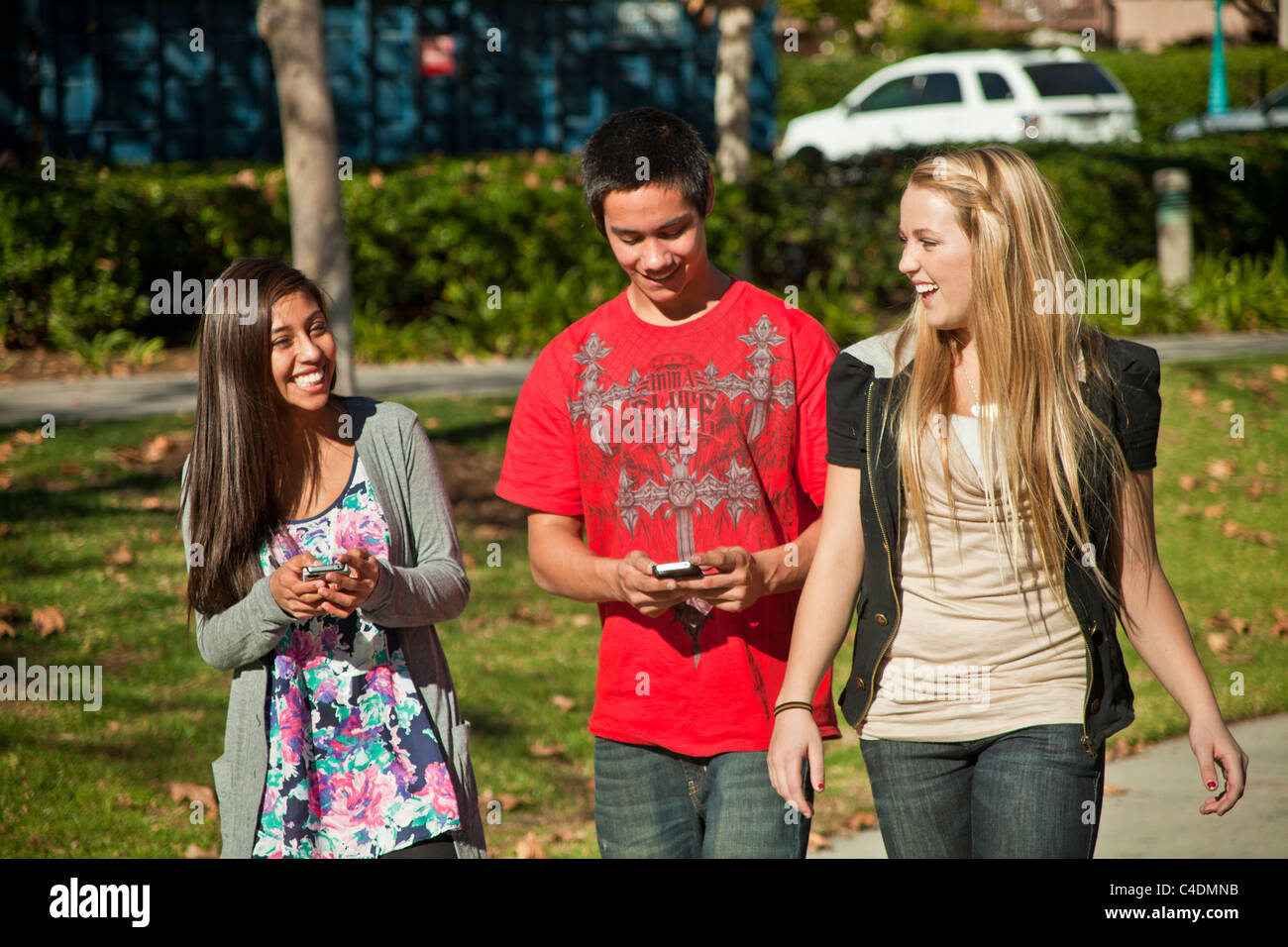 Glücklich lachende Multi Diverse American Indian, kaukasischen und Hispanic Volksgruppe von 3 drei Jugendliche zu Fuß zu Fuß mit iPhone Mobile Phone. HERR Stockfoto