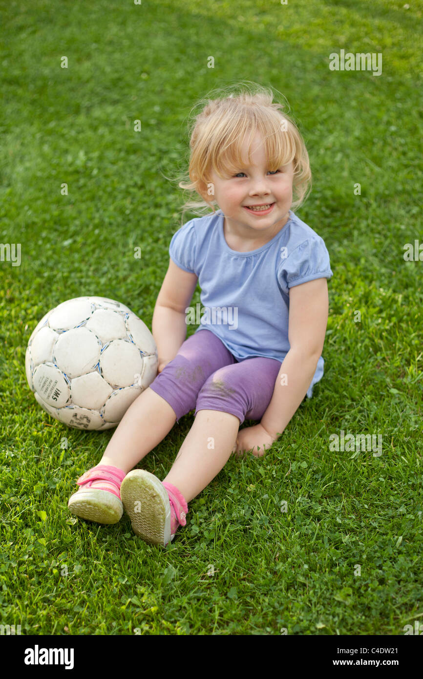 Lächelndes Mädchen, das auf Gras ruht und einen Fußball neben sich hat. Stockfoto