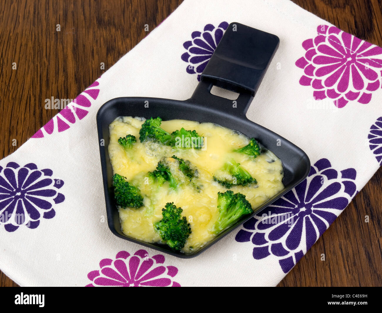 Raclettepfännchen mit Käse und Broccoli auf bunte Serviette Stockfoto