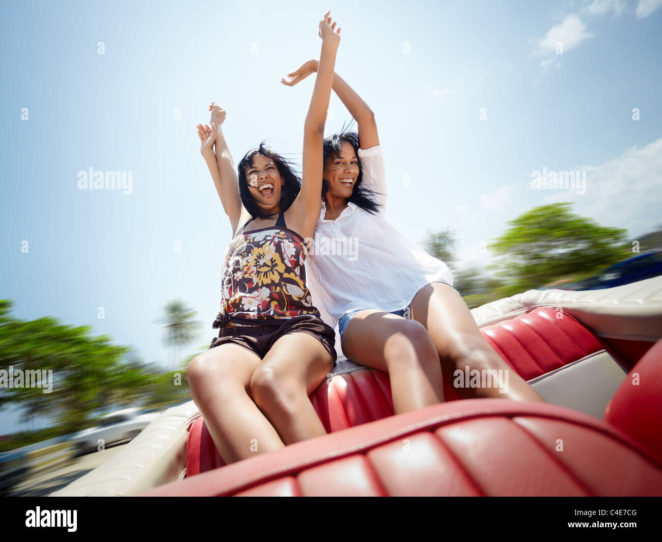 junge Erwachsene Brünette Twin Frauen sitzen im roten Cabrio und lachen. Horizontale Form, Vorderansicht, Textfreiraum Stockfoto