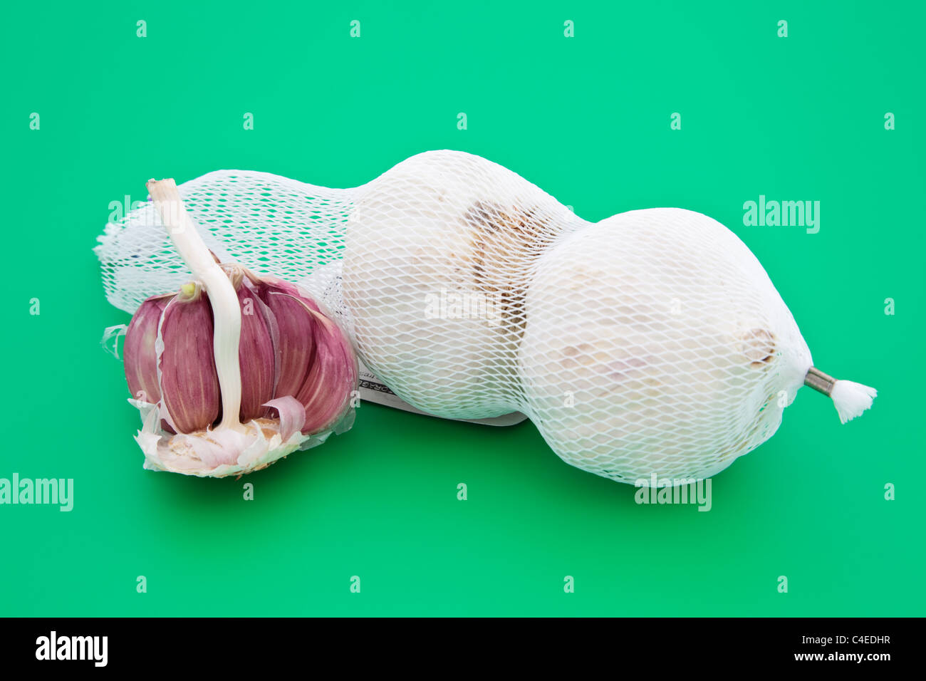 Zwei ganze Knoblauch Zwiebeln und eine Hälfte mit Nelken in einem Netz auf einem Schneidebrett grün Stockfoto