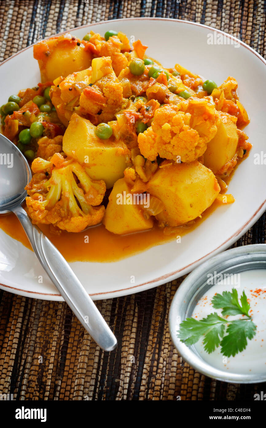 Indische vegetarische Curry aus Blumenkohl, Kartoffeln und Erbsen, serviert mit Joghurt hergestellt. Stockfoto