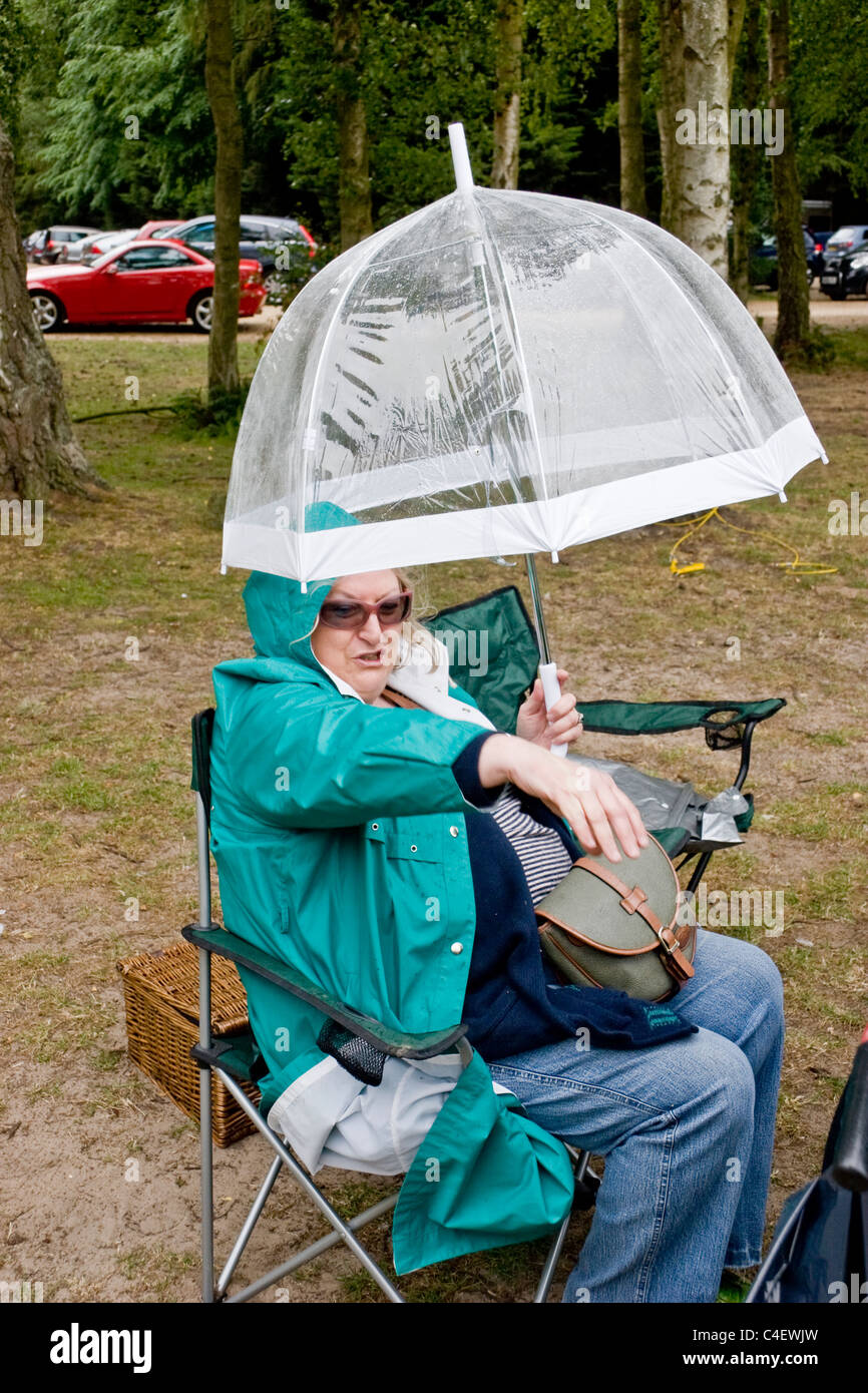 Reife Frau mit Regenschirm, Picknick in einem Park im Regen Stockfoto