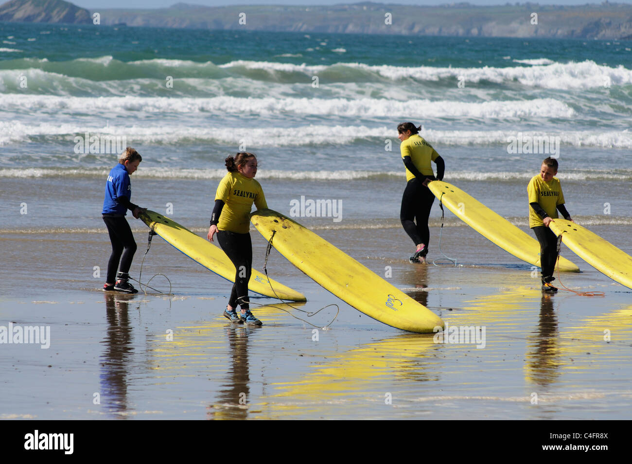 Schülerinnen und Schüler ziehen ihre Surfbretter ins Meer für Surfkurse Stockfoto