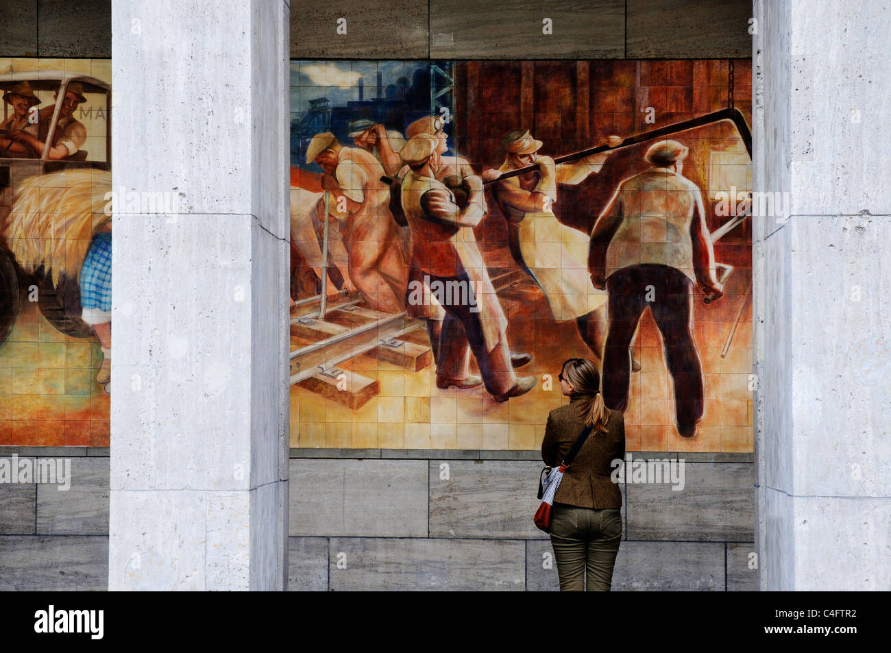 Eine Frau betrachten das sozialistische Wandbild der glückliche Arbeiter an der Wand des Bundesministeriums der Finanzen der Gebäude in ex-Ostberlin Stockfoto
