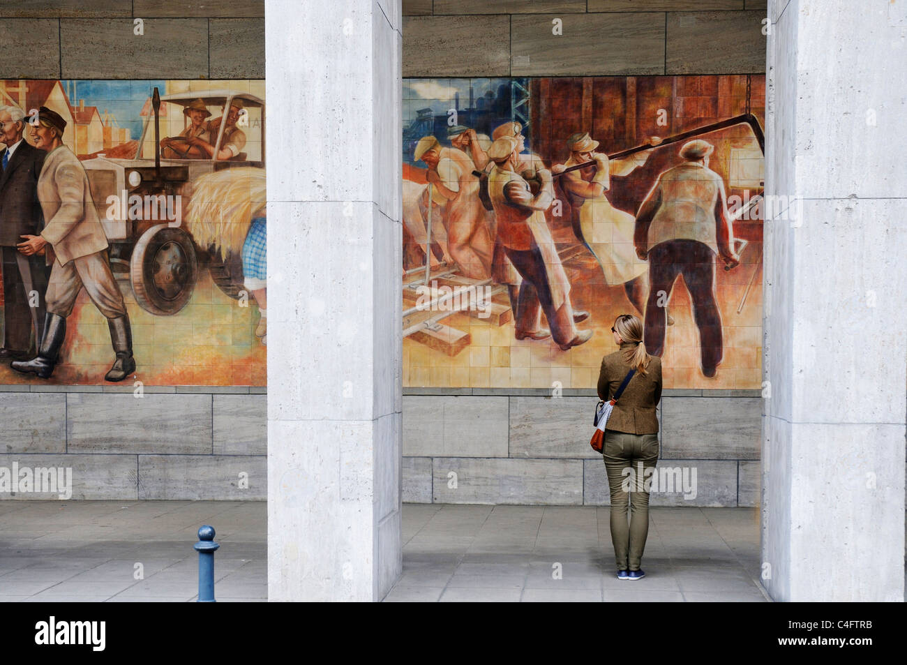 Eine Frau betrachten das sozialistische Wandbild der glückliche Arbeiter an der Wand des Bundesministeriums der Finanzen der Gebäude in ex-Ostberlin Stockfoto