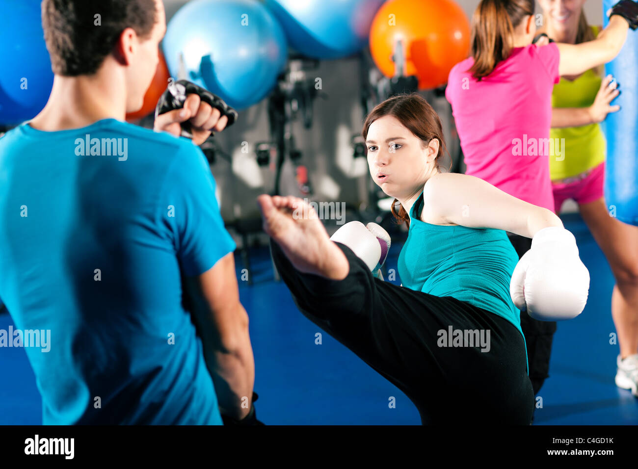 Kick-Boxer Frau treten ihr Trainer in einem sparring Session, im Hintergrund sind andere Boxer der Sandsack schlagen Stockfoto