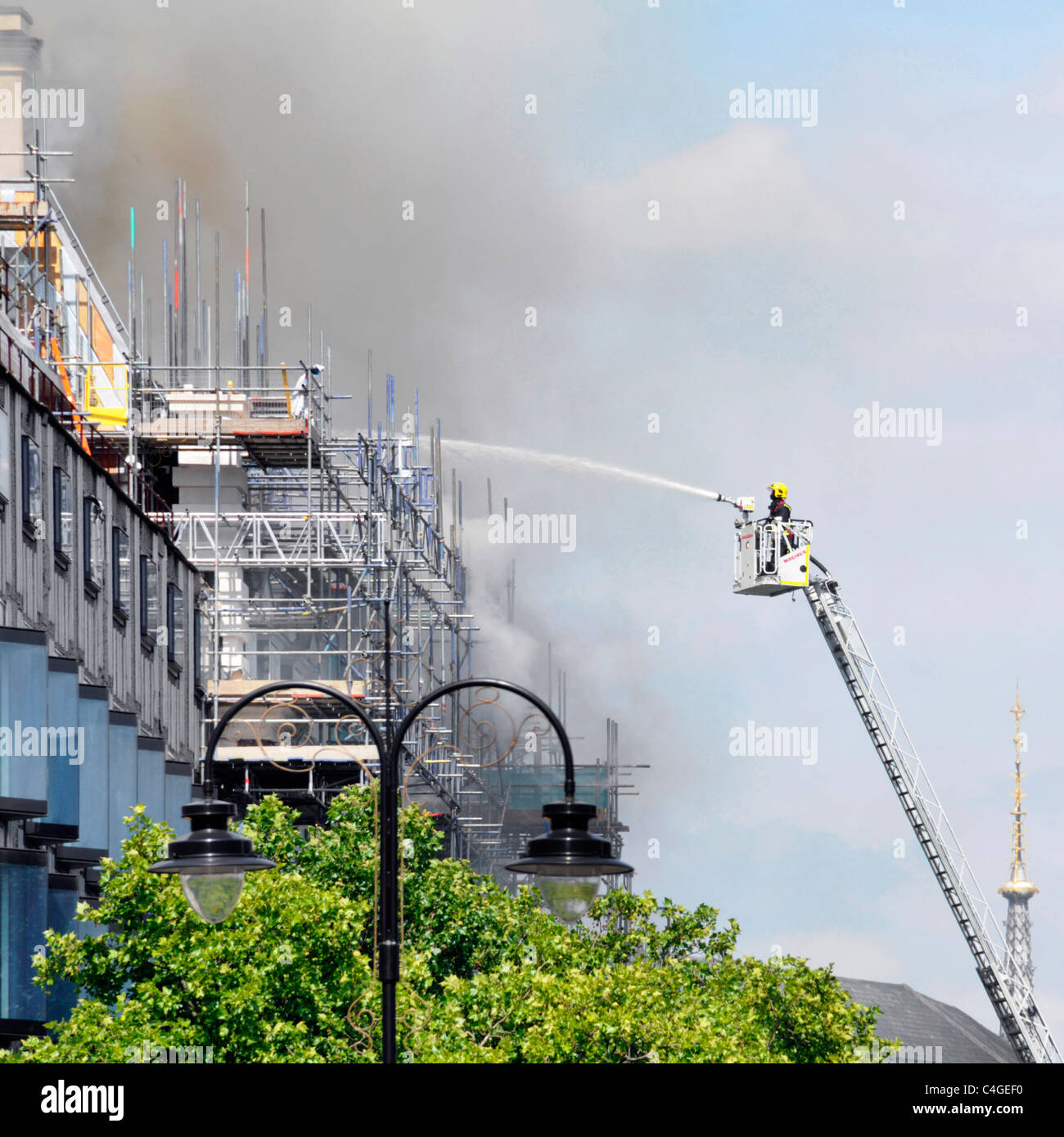 Feuerwehrmann auf der Zugangsplattform sprüht Wasser auf das Dachfeuer im Marconi House Umbau Baustelle am Strand London England UK Stockfoto