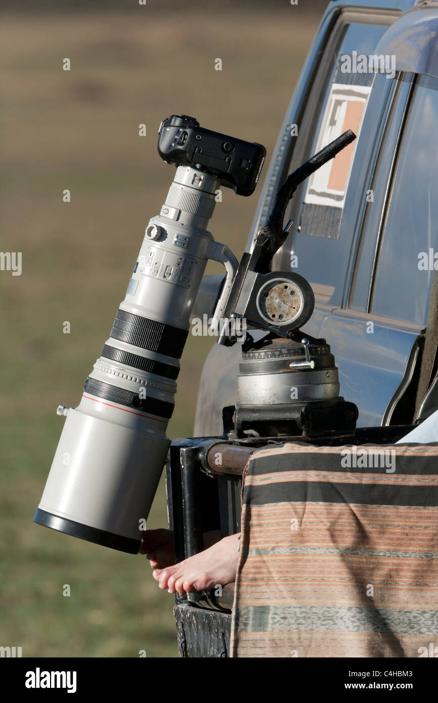 Der BBC Big Cat Diary Fotograf wartet in Kenia Masai Mara, Kamera- und Teleobjektiv auf Fahrzeug-Kamera über Fotografen nackten Füße Stockfoto