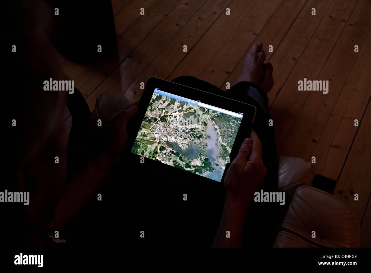 Mann sitzt in der dunklen beobachten GoogleEarth auf seinem Ipad Stockfoto
