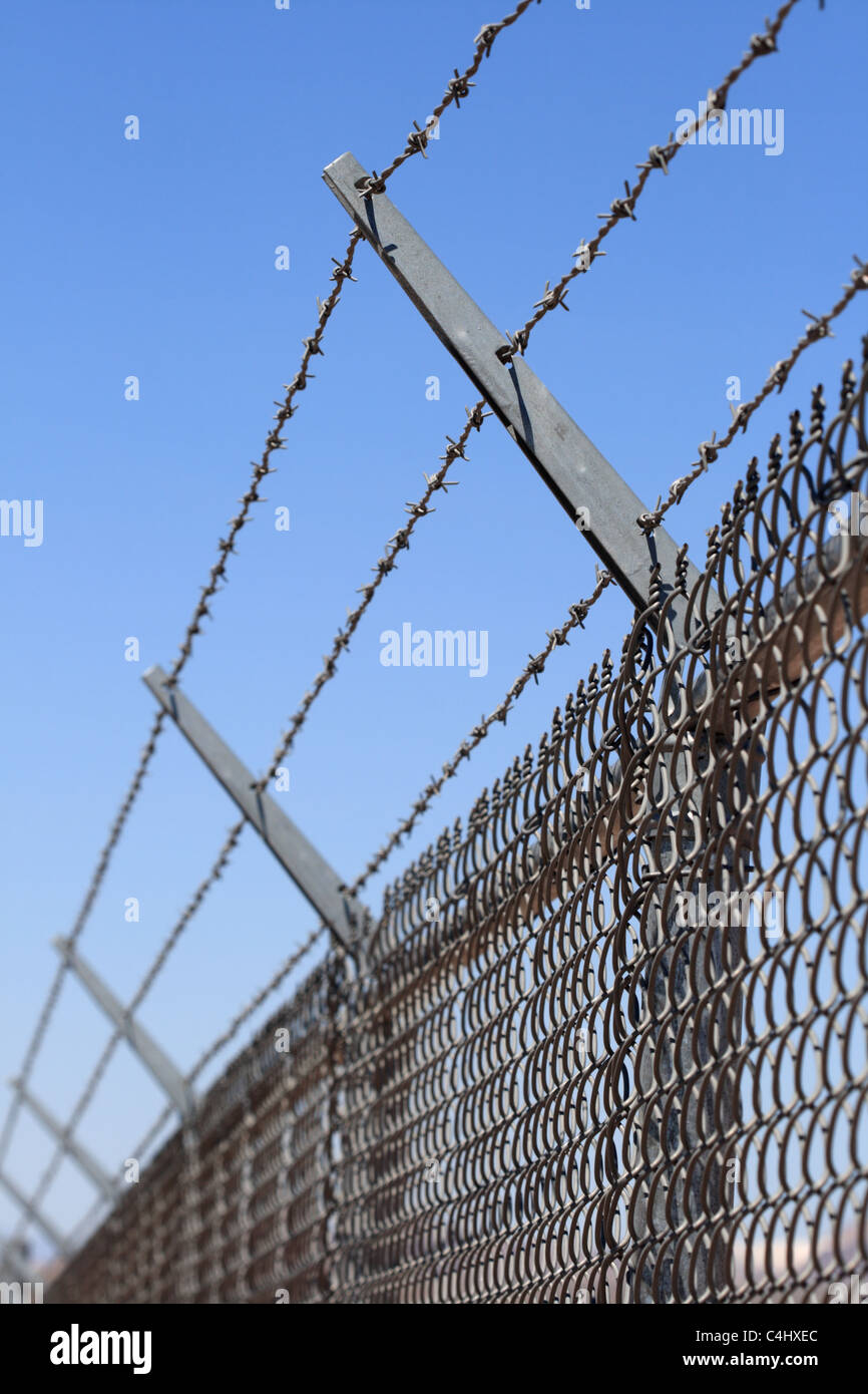 vertikales Bild von einer Sicherheit Maschendrahtzaun gekrönt mit drei Strängen aus Stacheldraht Stockfoto