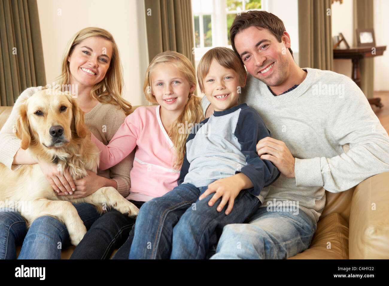 Glückliche junge Familie auf Sofa hält einen Hund Stockfoto