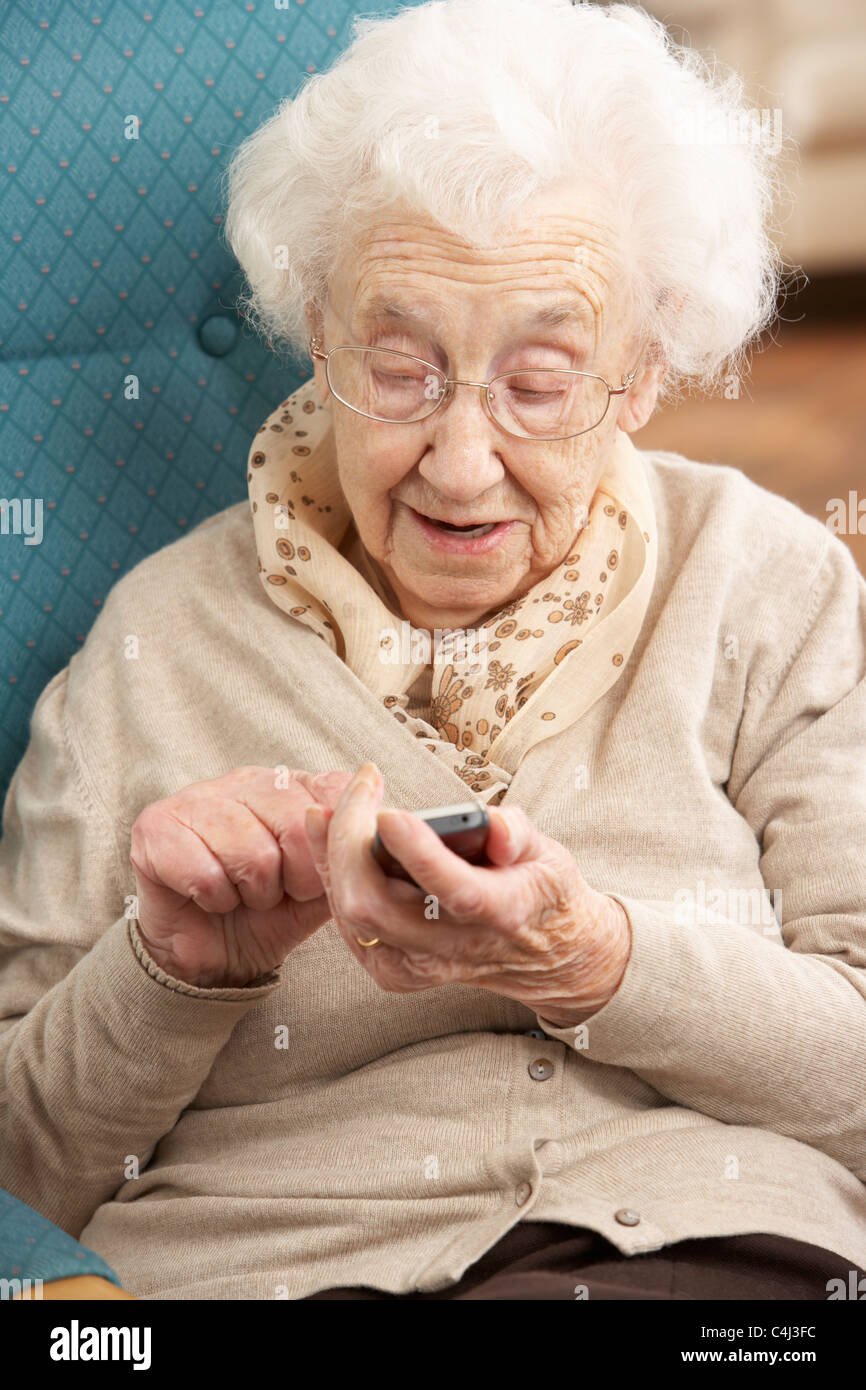 Ältere Frau Einwahl-Nummer auf Handy zu Hause im Sessel sitzen Stockfoto