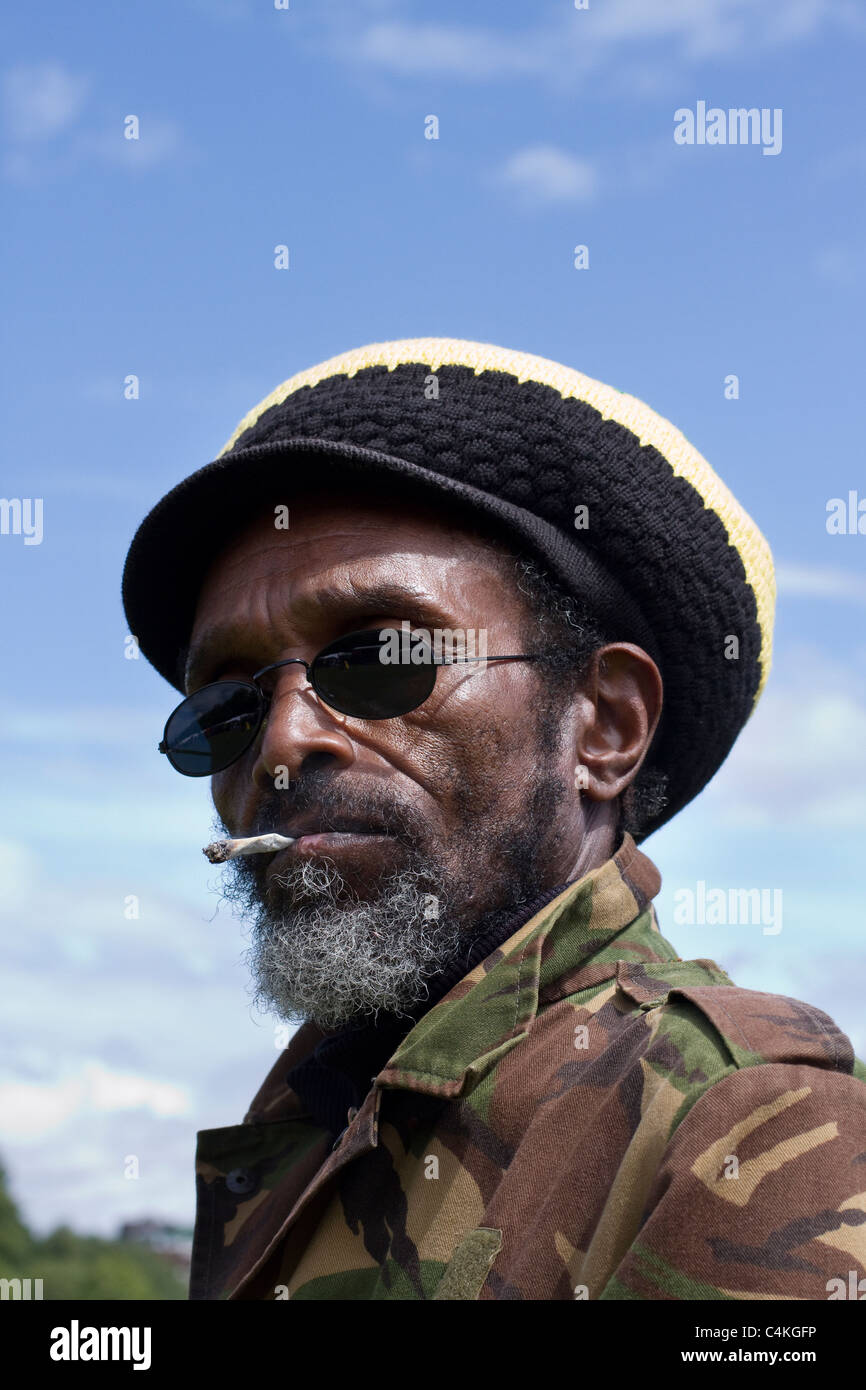 Tam (MR) Rauchen & tragen Rasta Kammgarn Motorhaube, Rasta und Reggae headwear einschließlich Hüte, Mützen, Caps, strotzt, Tams, fedoras, Schals und dreadlock Perücke Hüte in Afrika Oye Event in Sefton Park Liverpool UK größte freie Afrikanische Musik Festival Stockfoto