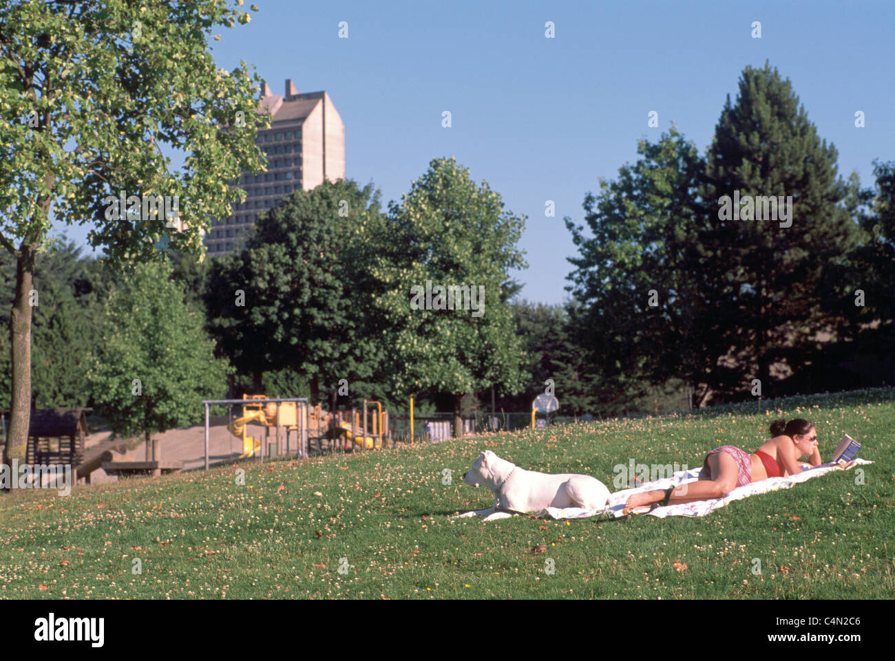 Frau mit Hund auf einer Decke Sonnenbaden und Lesen eines Buches in einer Urban Park Stockfoto