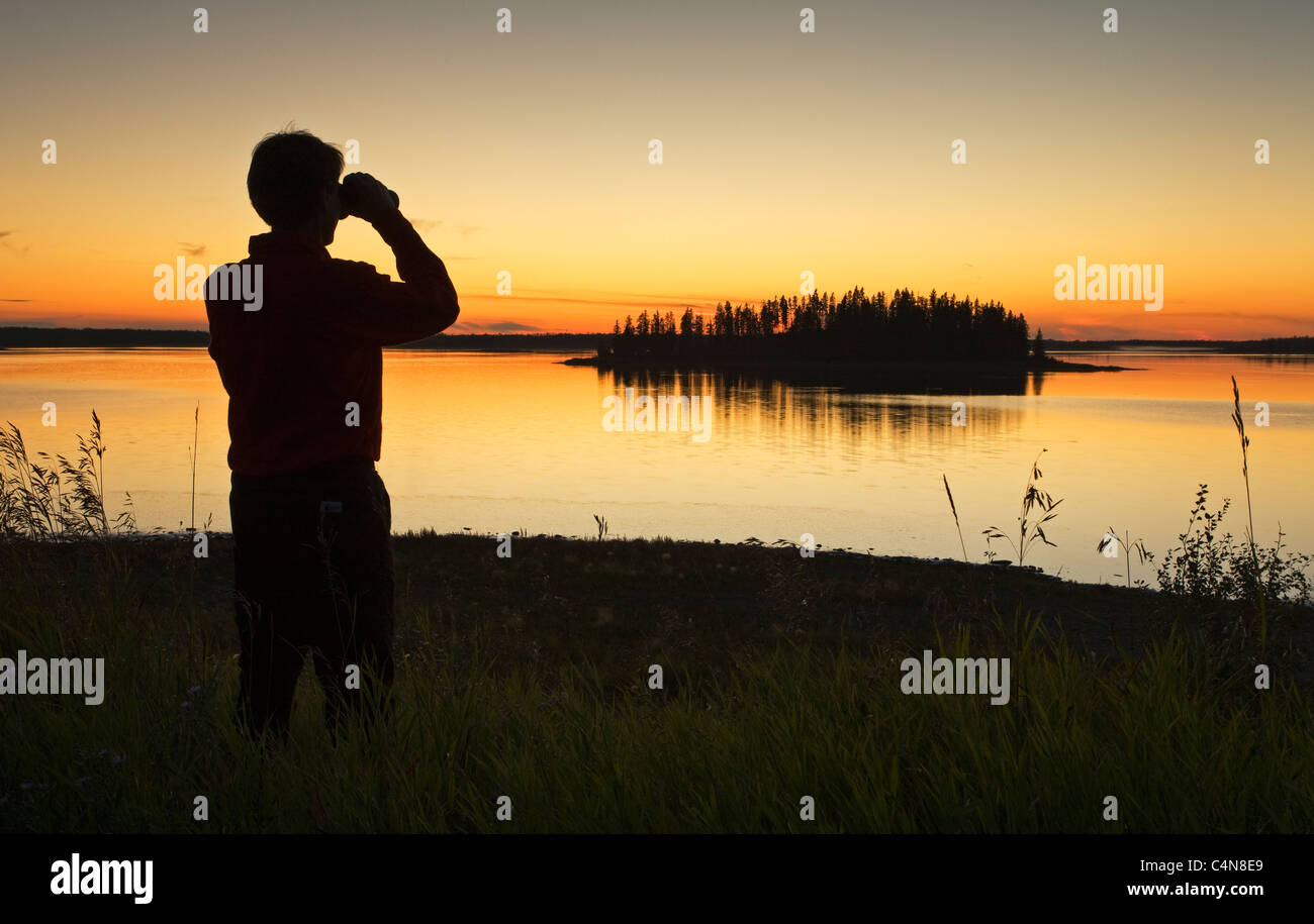 Mittleren Alters männlichen Wanderer Blick auf Astotin Lake mit dem Fernglas in der Abenddämmerung, Elk Island Park, Alberta, Kanada. Stockfoto