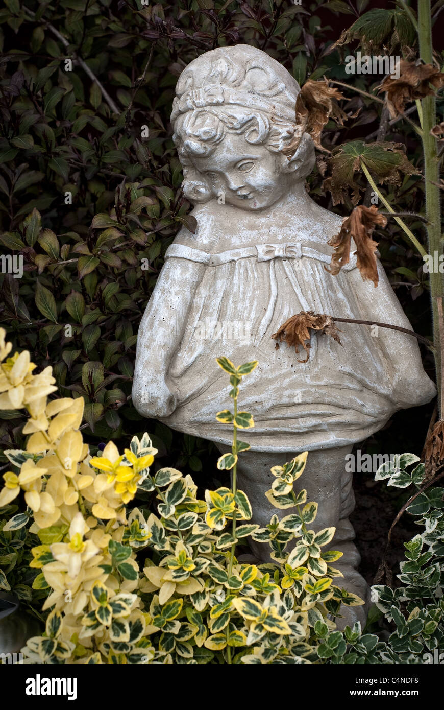Eine steinerne Statue eines jungen Mädchens steht unter dem Laub eines vernachlässigten Garten Stockfoto