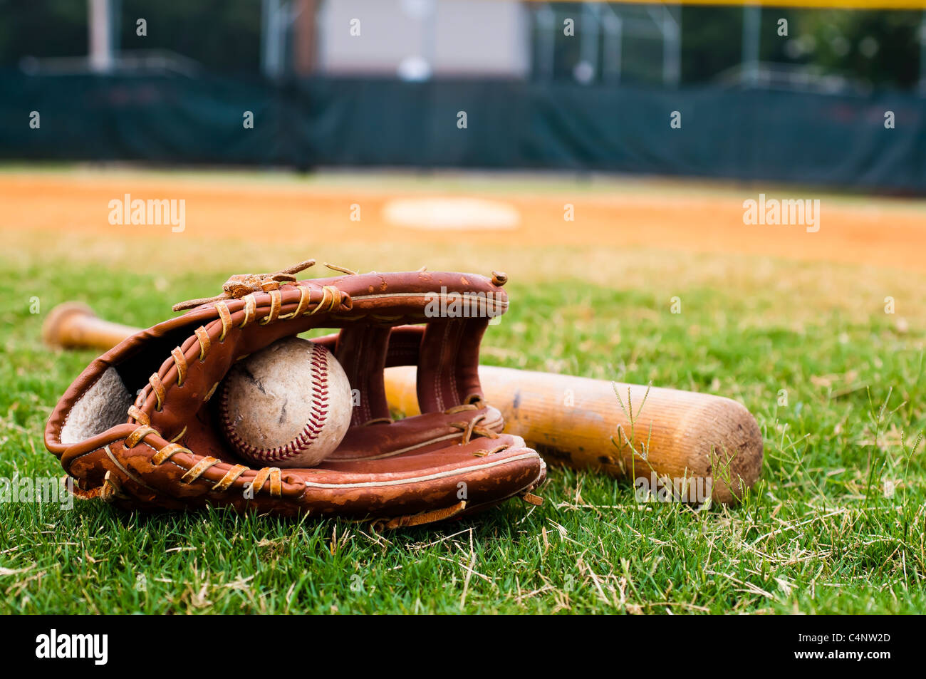 Baseball, Handschuh und Fledermaus auf Feld mit Sockel und Feldspieler im Hintergrund. Stockfoto