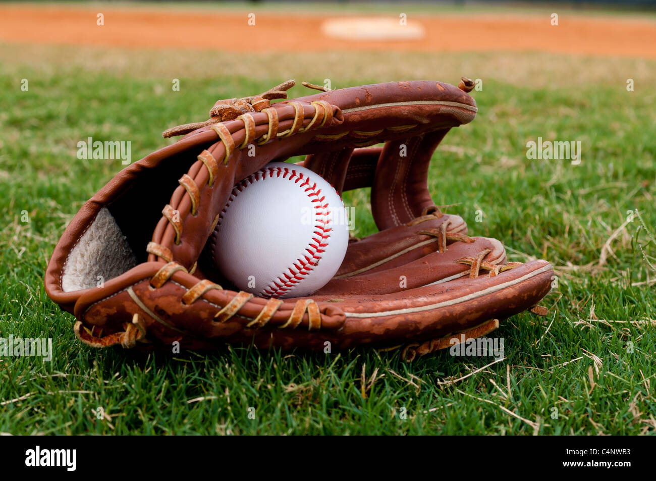 Baseball und Handschuh auf Feld mit Sockel und Feldspieler im Hintergrund. Stockfoto