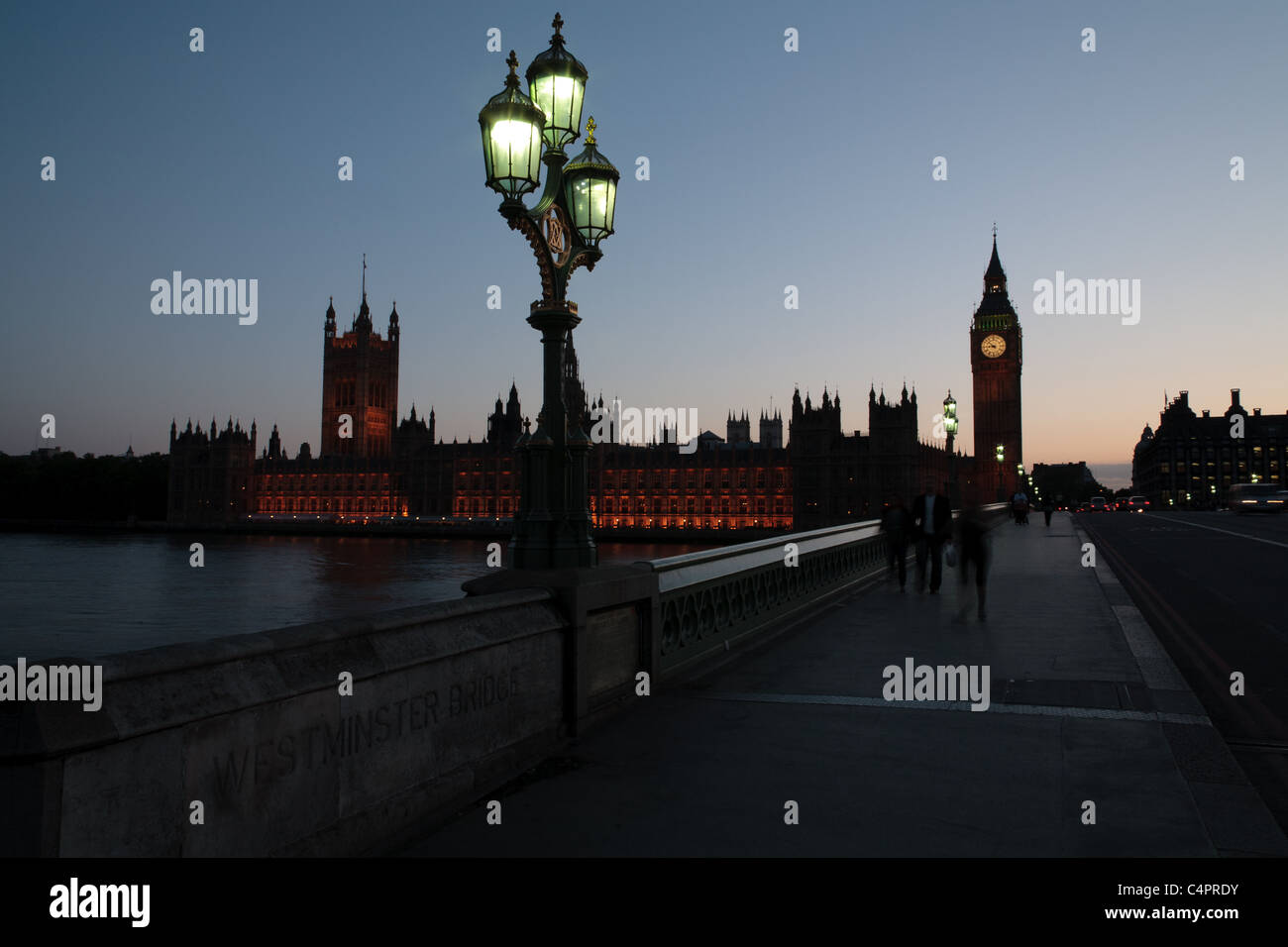 Eine untergehende Sonne Silhouetten der Houses of Parliament und Big Ben in London, England. Verwischte die Menschen gehen über die Brücke. Stockfoto