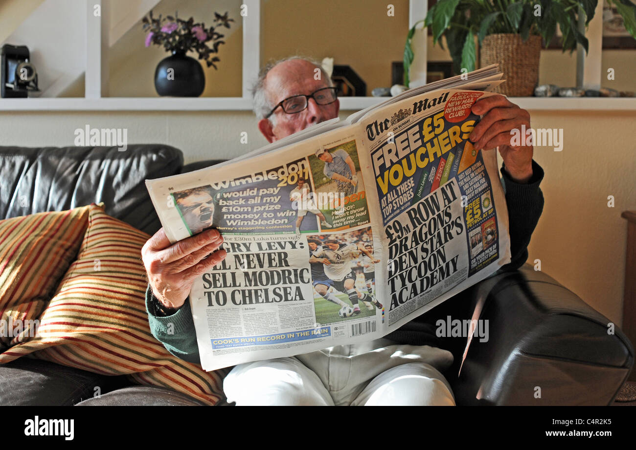 Mann Mitte der Achtziger, der am Sonntag eine nationale Zeitung The Mail auf einem Sofa im Wohnzimmer in Großbritannien las Stockfoto