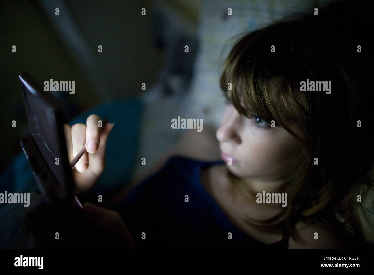 13-Year-Old Girl spielt mit ihrem tragbaren Spielsystem im Bett Stockfoto