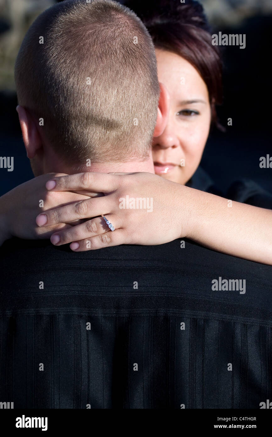 Eine hübsche junge Frau schmiegt sich an ihren Ehemann oder Verlobten. Geringe Schärfentiefe mit Fokus auf die Diamant-Verlobungsring. Stockfoto