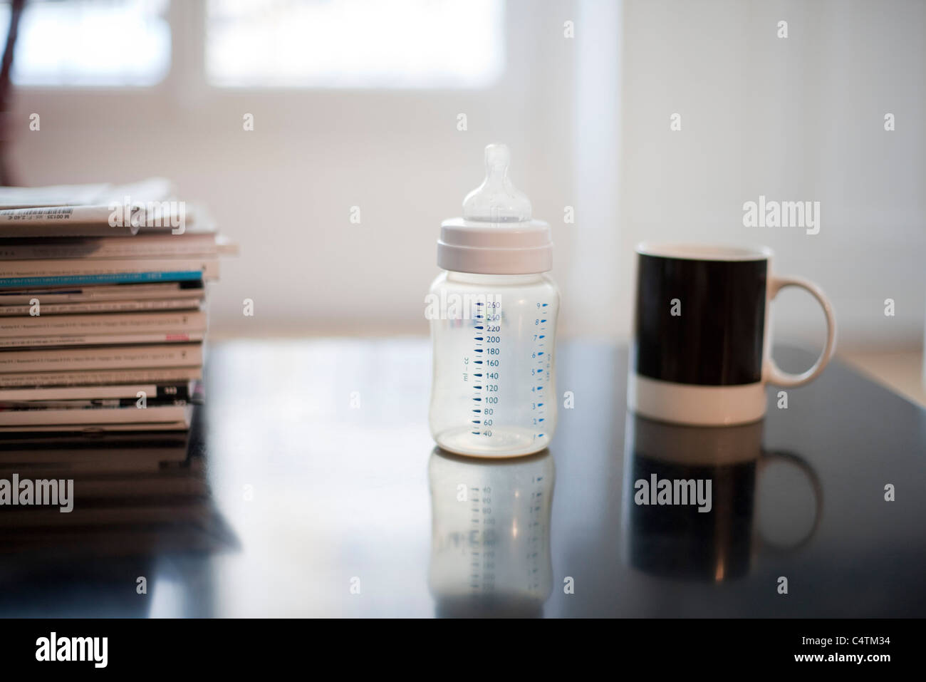 Babyflasche, Kaffeetasse und Stapel Zeitschriften Stockfoto