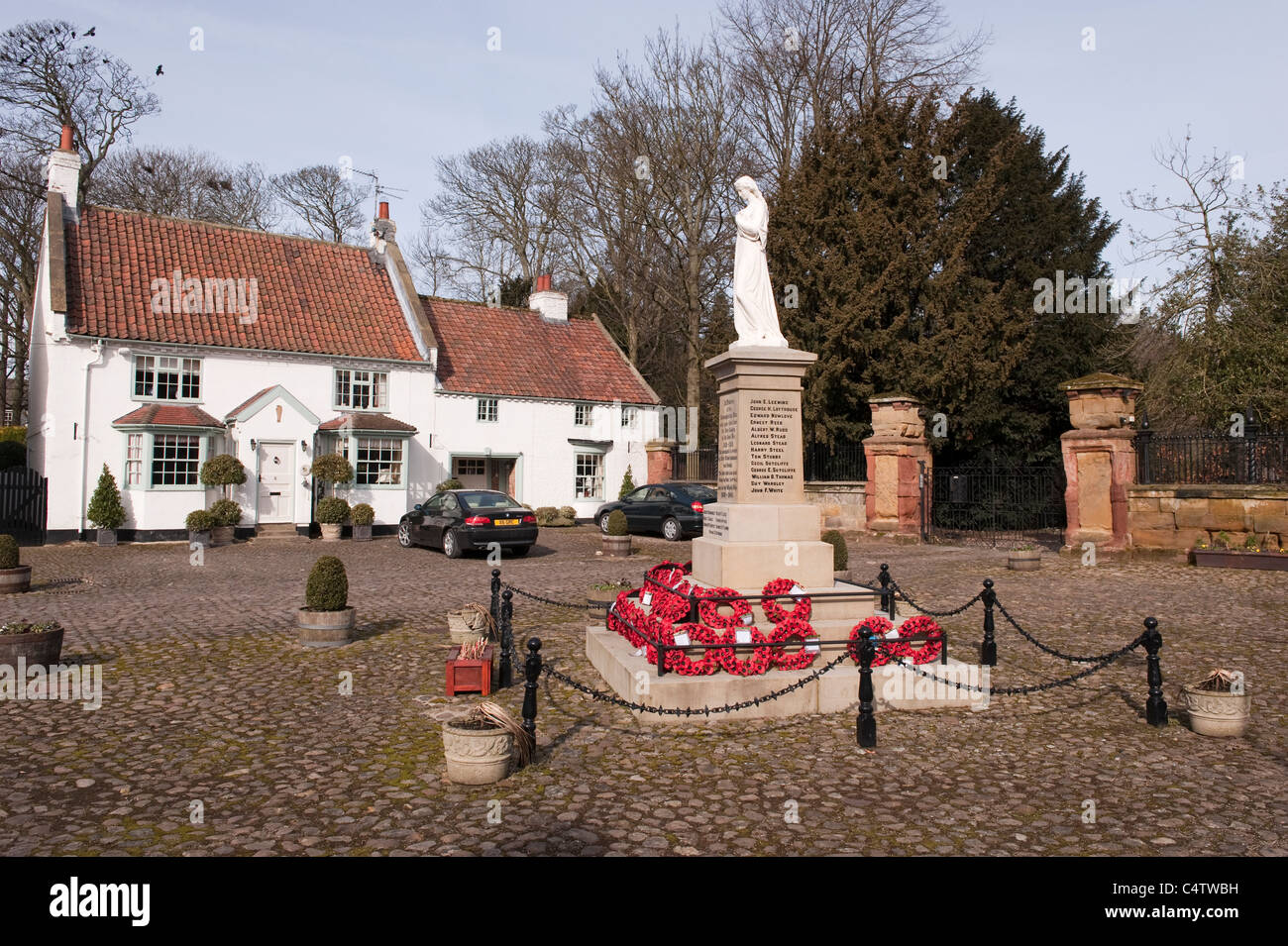 Rote Mohnkränze, die am Fuße des Kriegsdenkmals des 1. Und 2. Weltkriegs in einer attraktiven ländlichen Stadt - Kopfsteinpflaster Hall Square, Boroughbridge, North Yorkshire, England, Großbritannien, gelegt werden. Stockfoto